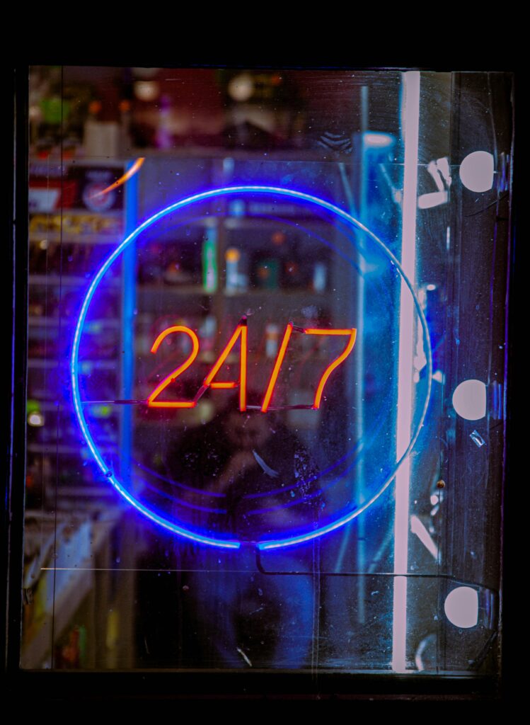 pexels photo 10901316 10901316 Vibrant neon blue and red 24/7 sign glowing in a shop window at night, creating a bustling urban vibe.